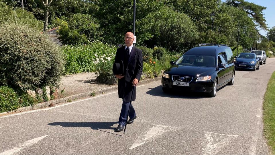 A person walking ahead of hearses at a funeral