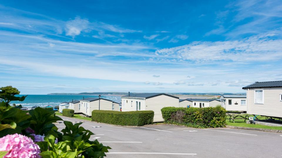 A view of a beach in the background of a holiday park featuring holiday homes in the foreground