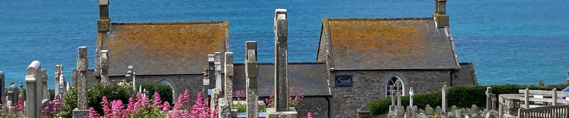 A view of headstones leading down hill towards the chapel of rest and the sea beyond 